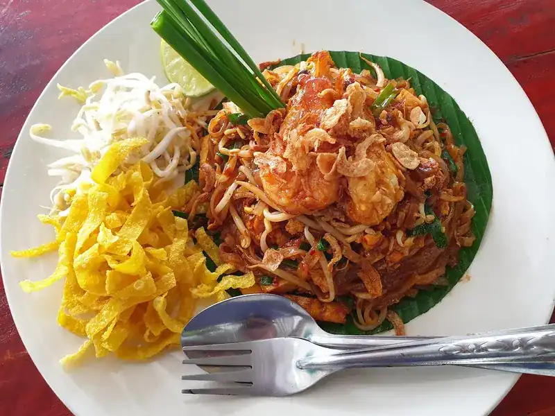 Pad thai with prawns on a banana leaf, with egg strips, bean sprouts, chives and lime
