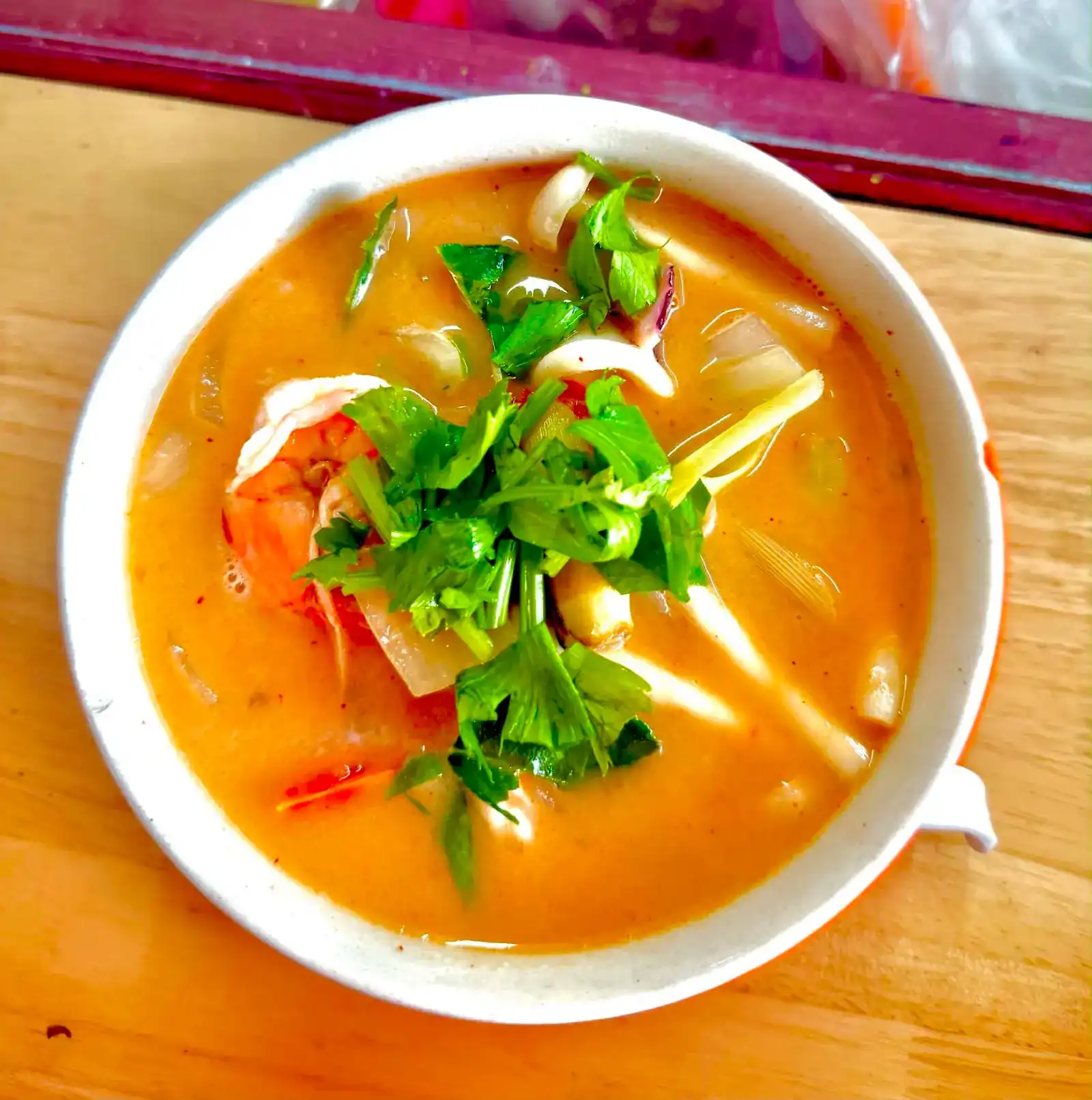 Creamy tom yum with prawn, squid and coriander in a white bowl