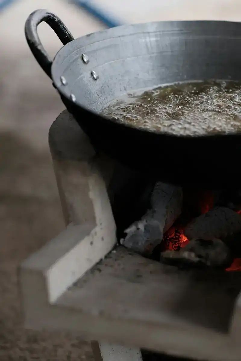 A steel wok bubbling over glowing charcoal on a clay stove