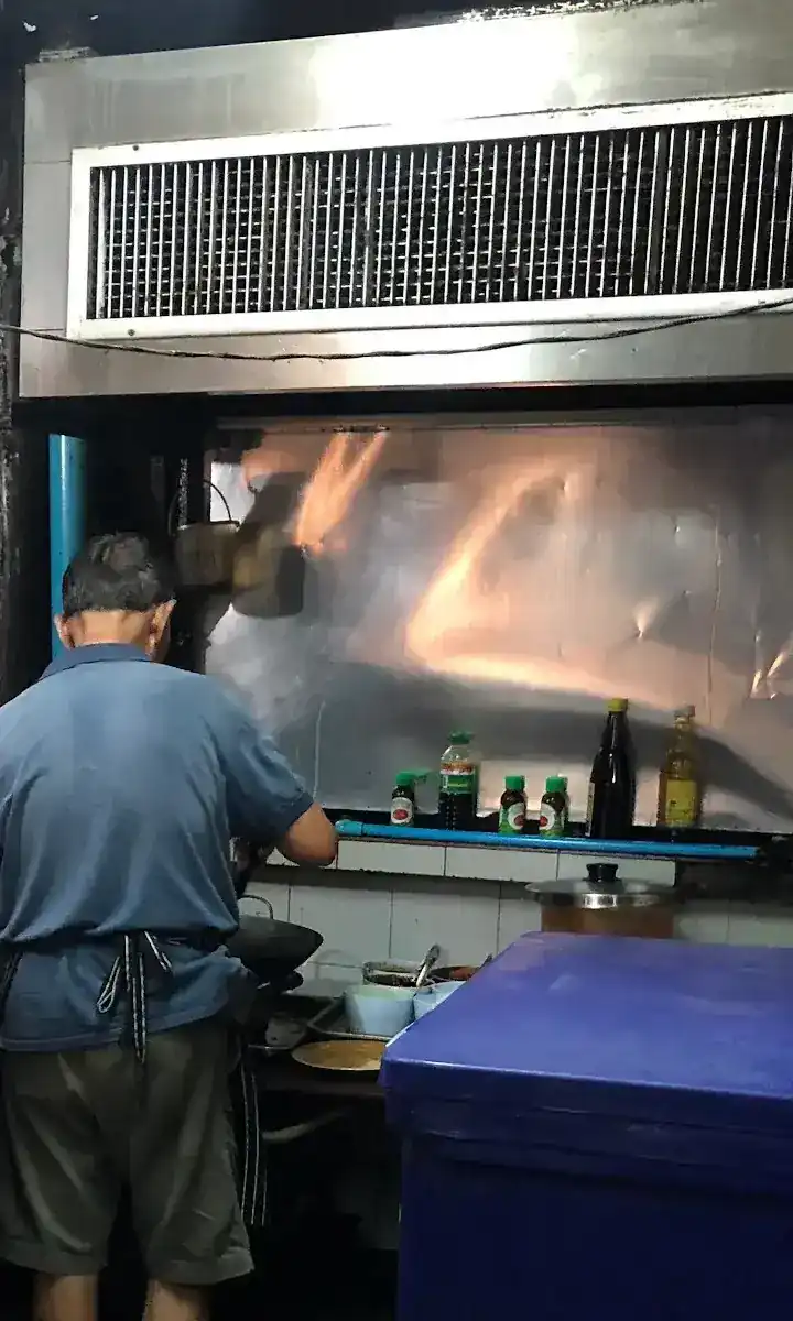 The cook at the wok under the steel hood, seen from behind