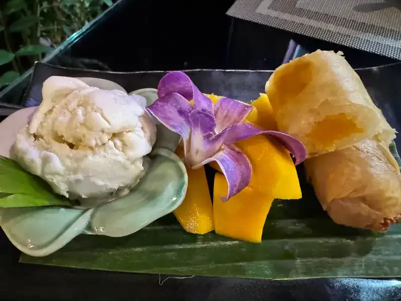 Ice cream, fresh mango and crisp fried rolls with a purple orchid on banana leaf