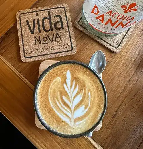 A latte with leaf art beside a Vida Nova cork coaster