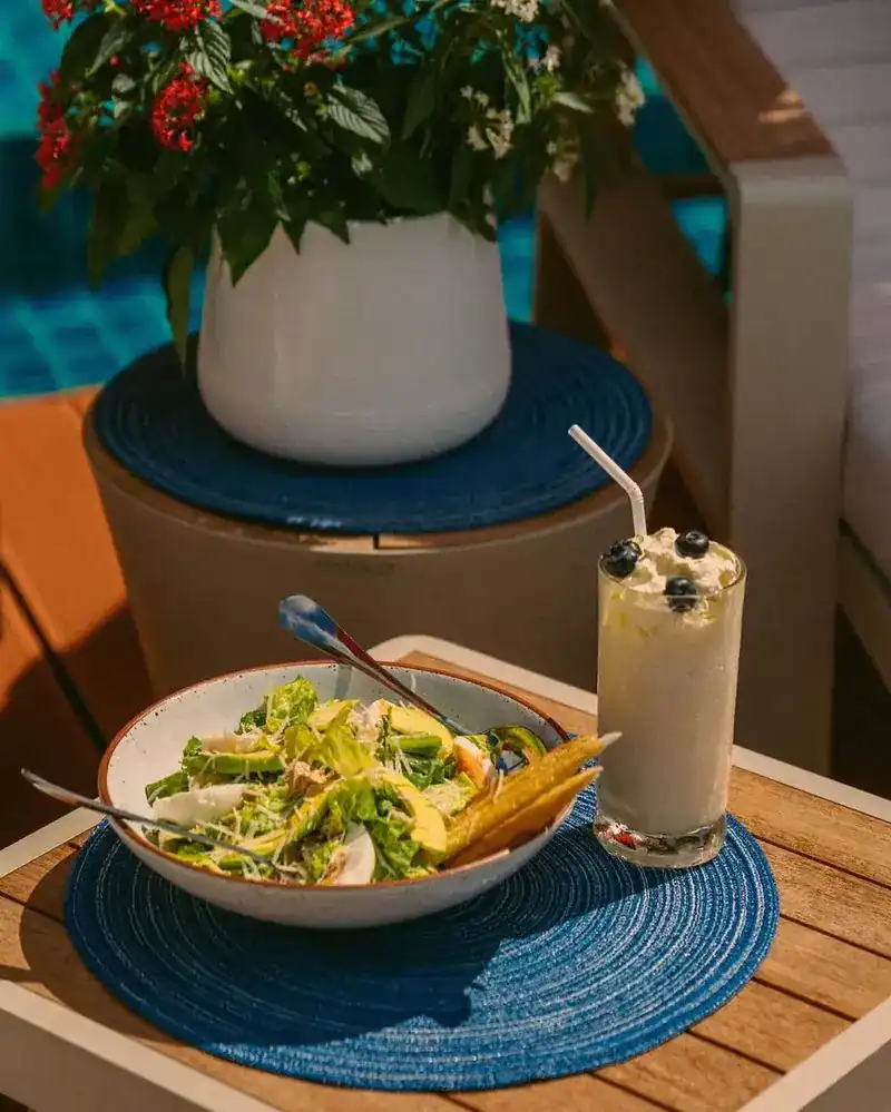 A salad and a smoothie on a small table beside the pool