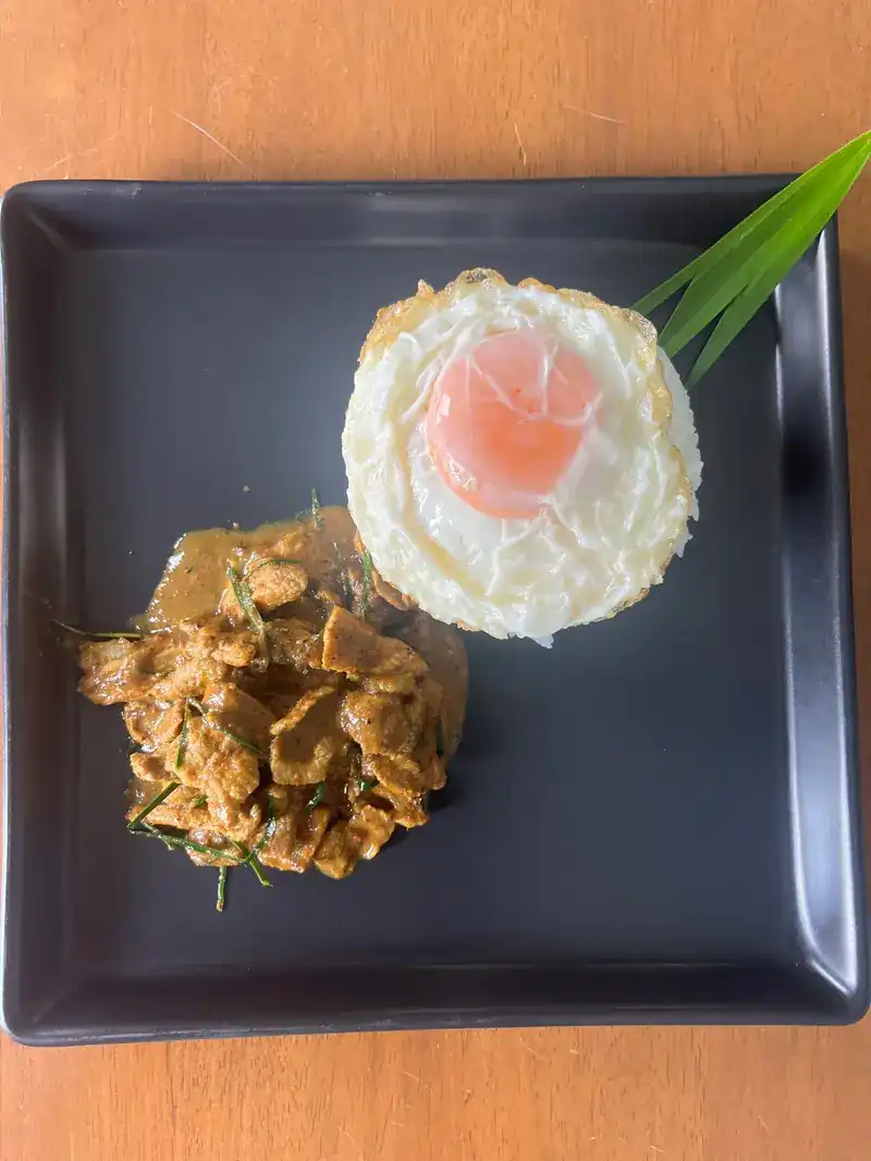 Meat in a thick curry sauce next to a fried egg on a dark plate