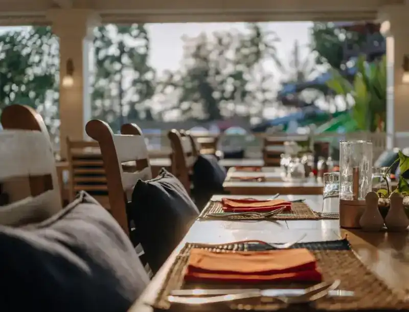 Long tables set with orange napkins on the open terrace, palms beyond