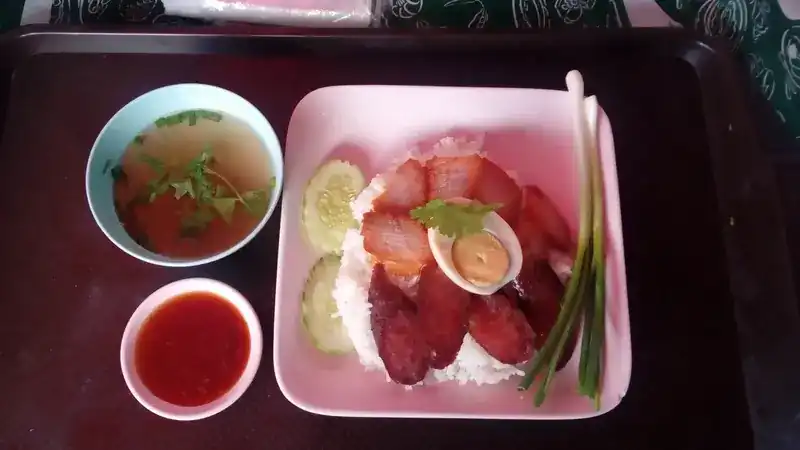 Red pork and Chinese sausage over rice with half an egg and cucumber, with a cup of soup and a dish of sauce