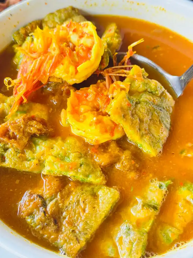 A bowl of yellow curry with prawns and pieces of omelette