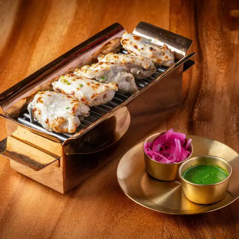 Chicken charred from the tandoor on a copper grill, with pickled onion and green chutney