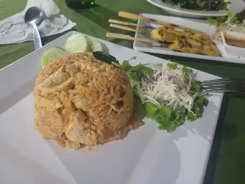 A dome of fried rice with cucumber and salad, satay skewers behind it