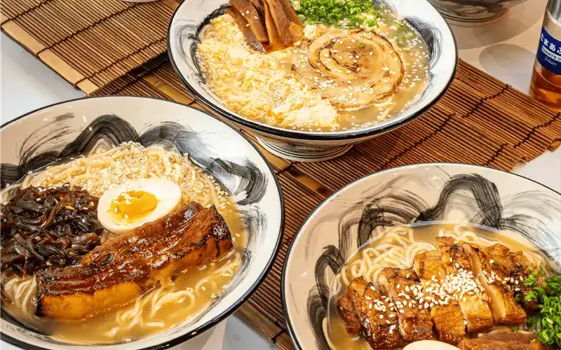 Three bowls of ramen in golden broth on bamboo mats