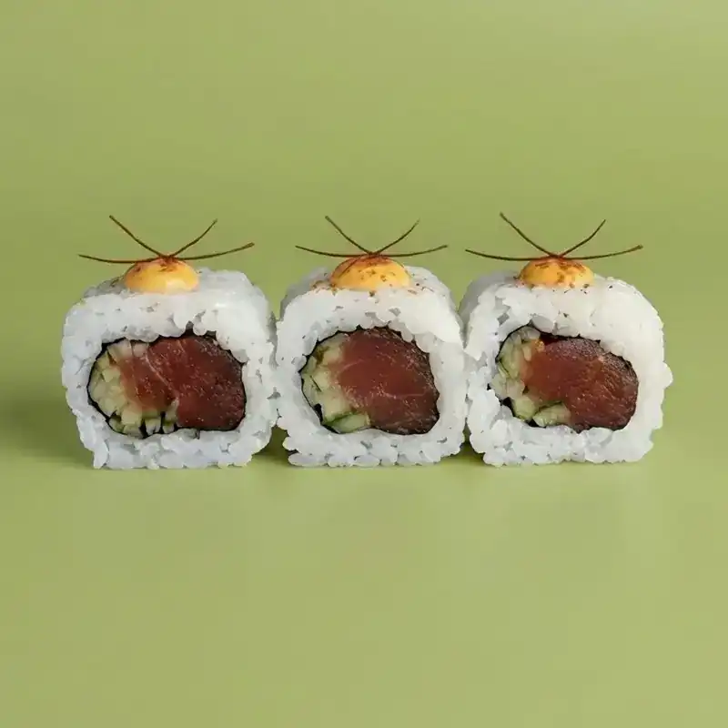 Three pieces of spicy tuna roll with chilli threads on a green background