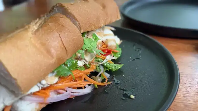 A baguette filled with herbs, carrot, red onion and chilli