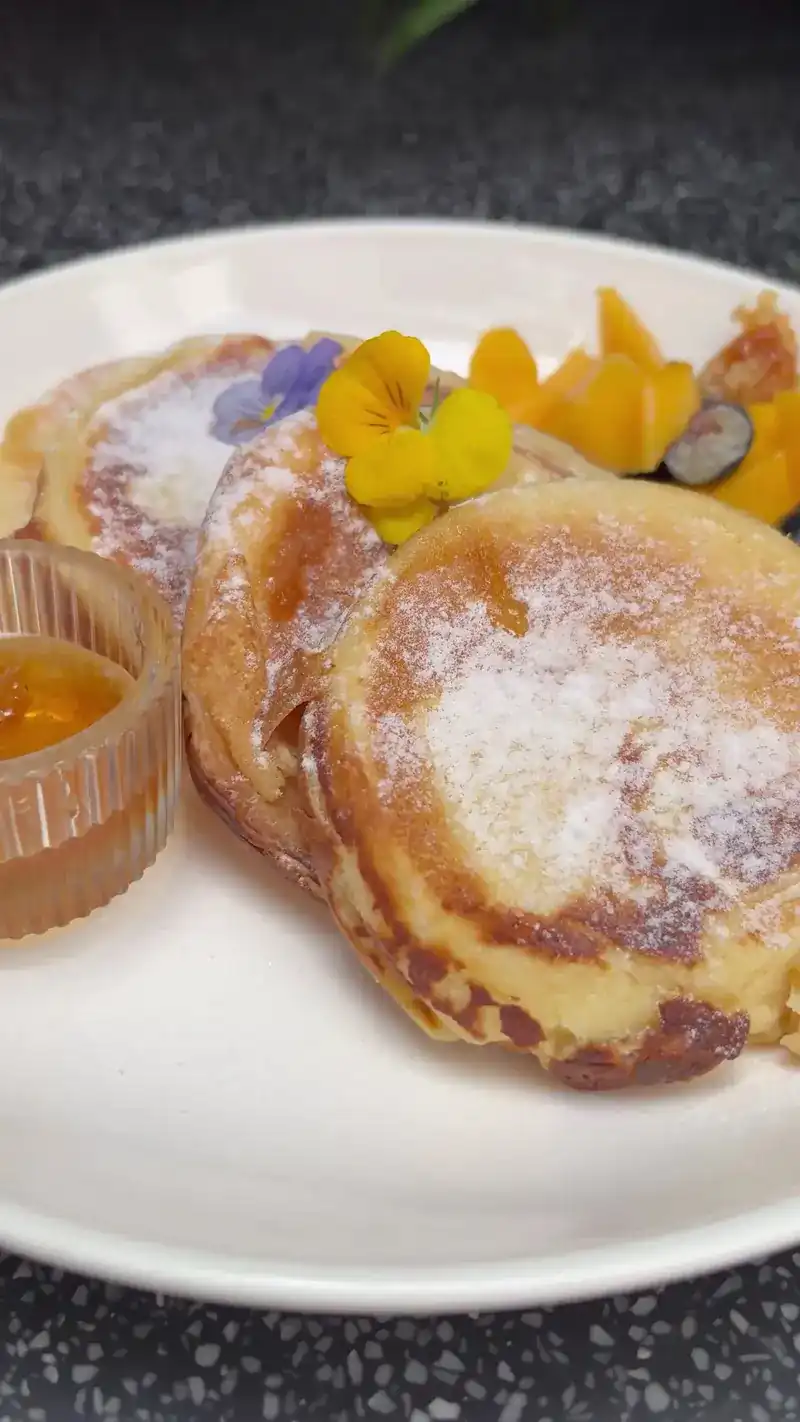 Ricotta pancakes dusted with sugar, with fruit, edible flowers and a little jar of sauce