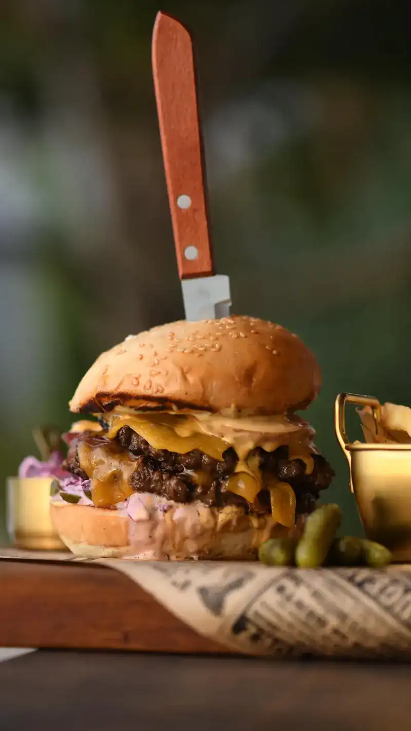 A tall cheeseburger with a knife through the bun