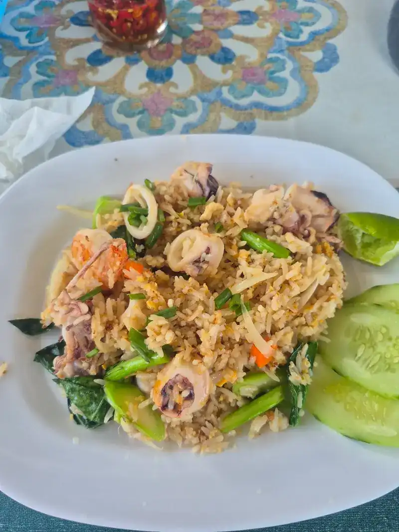 Fried rice with squid, prawns and Chinese kale, lime and cucumber on the side, a jar of chilli sauce behind