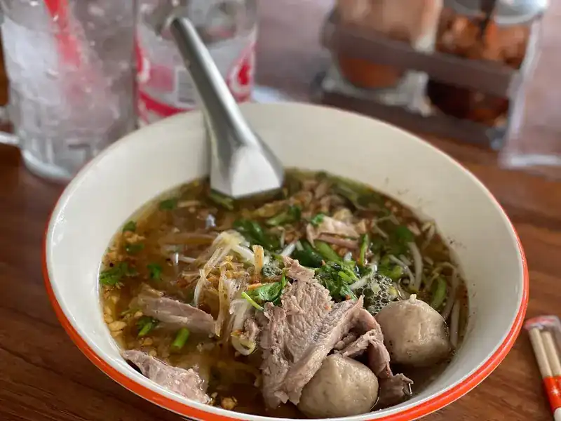 A bowl of noodle soup with sliced meat and meatballs