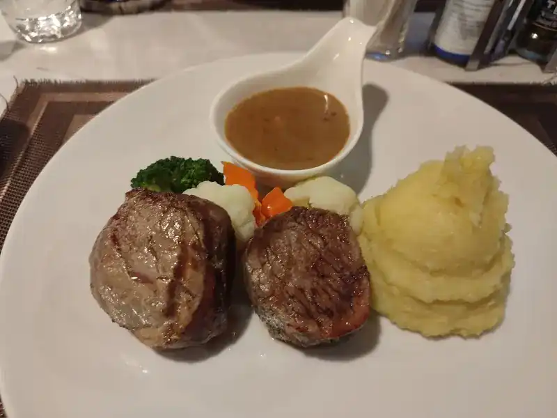 Two steak medallions with mashed potato, vegetables and a small jug of sauce