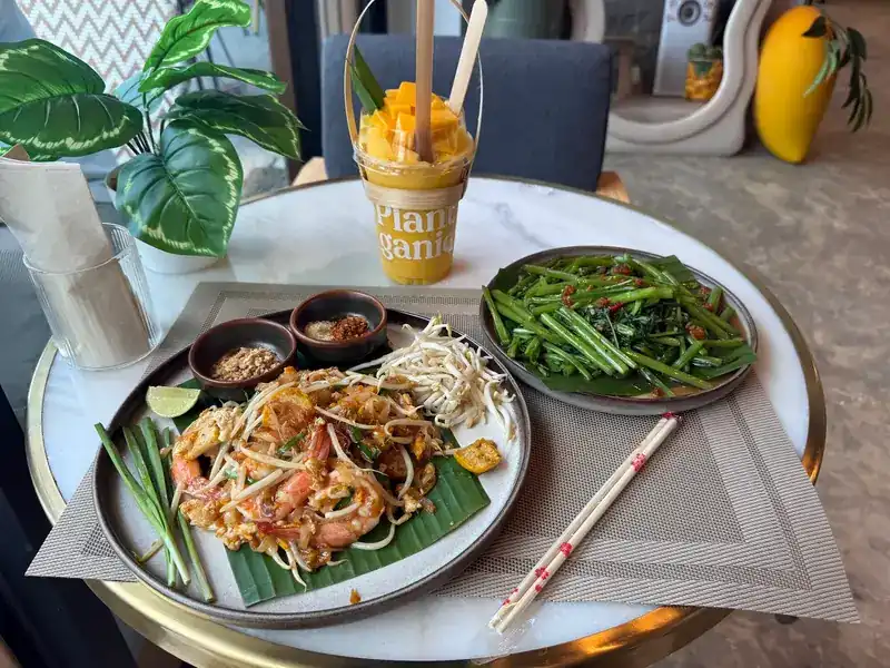 Pad thai with shrimp, stir-fried greens and a mango drink on a marble table
