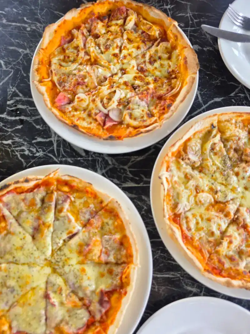 Three pizzas on white plates on a black marble table