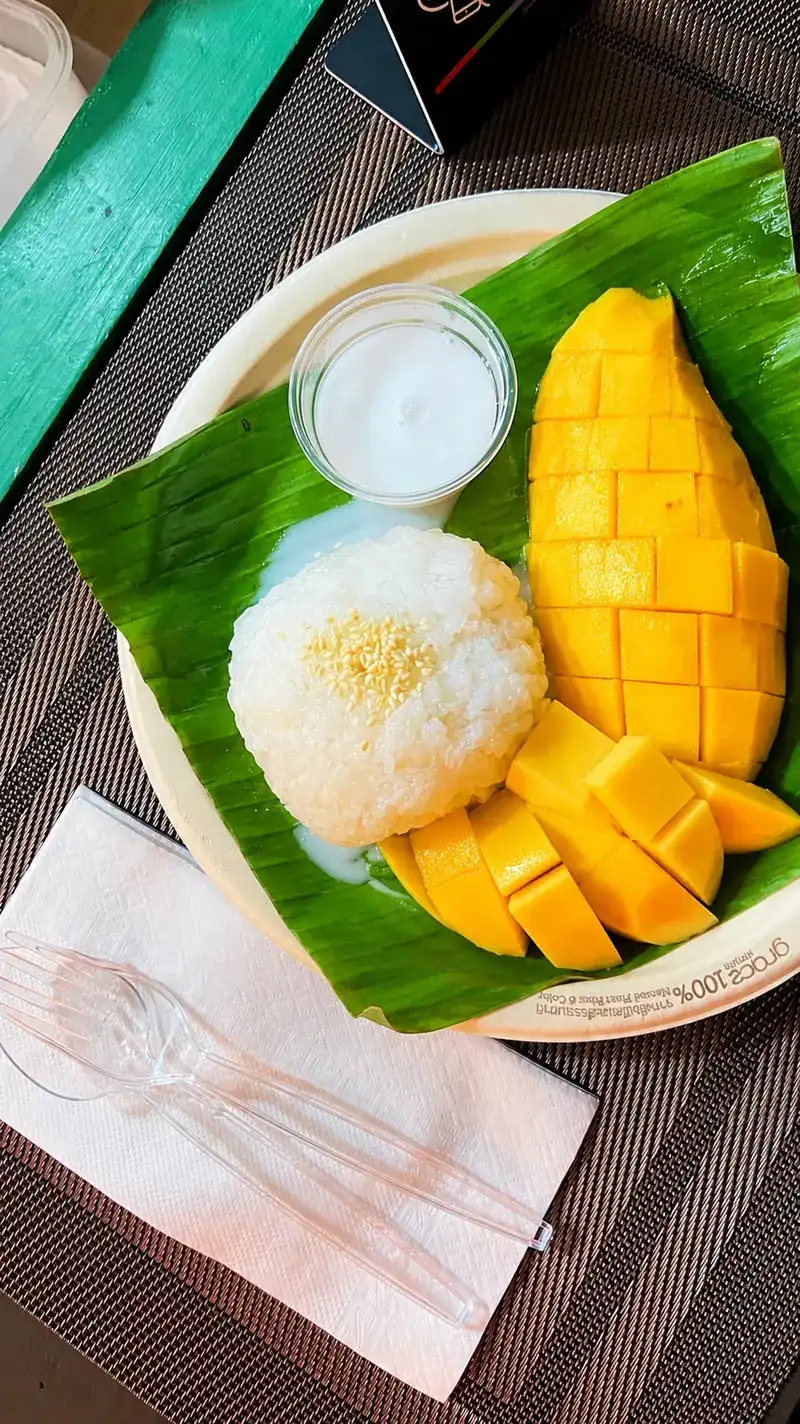 Mango sticky rice on a banana leaf with a cup of coconut cream