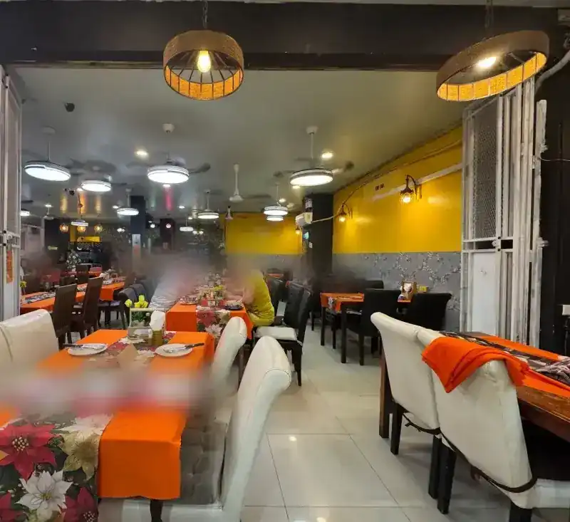 The dining room: orange tablecloths with flowered runners, white chairs, ceiling fans and a yellow wall
