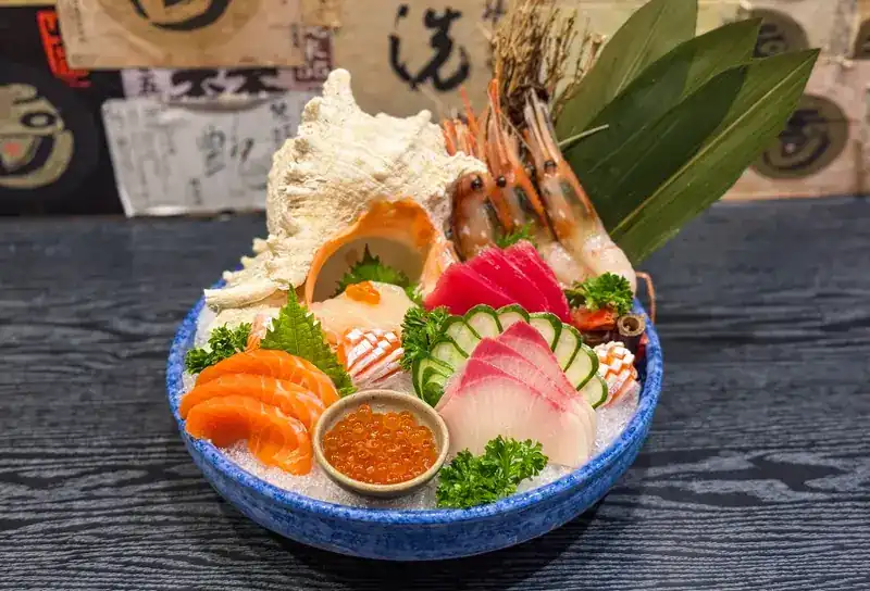 A blue bowl of sashimi, prawns and salmon roe on crushed ice