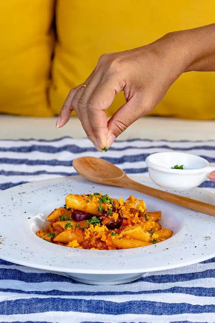 A hand sprinkling fresh herbs over a plated dish