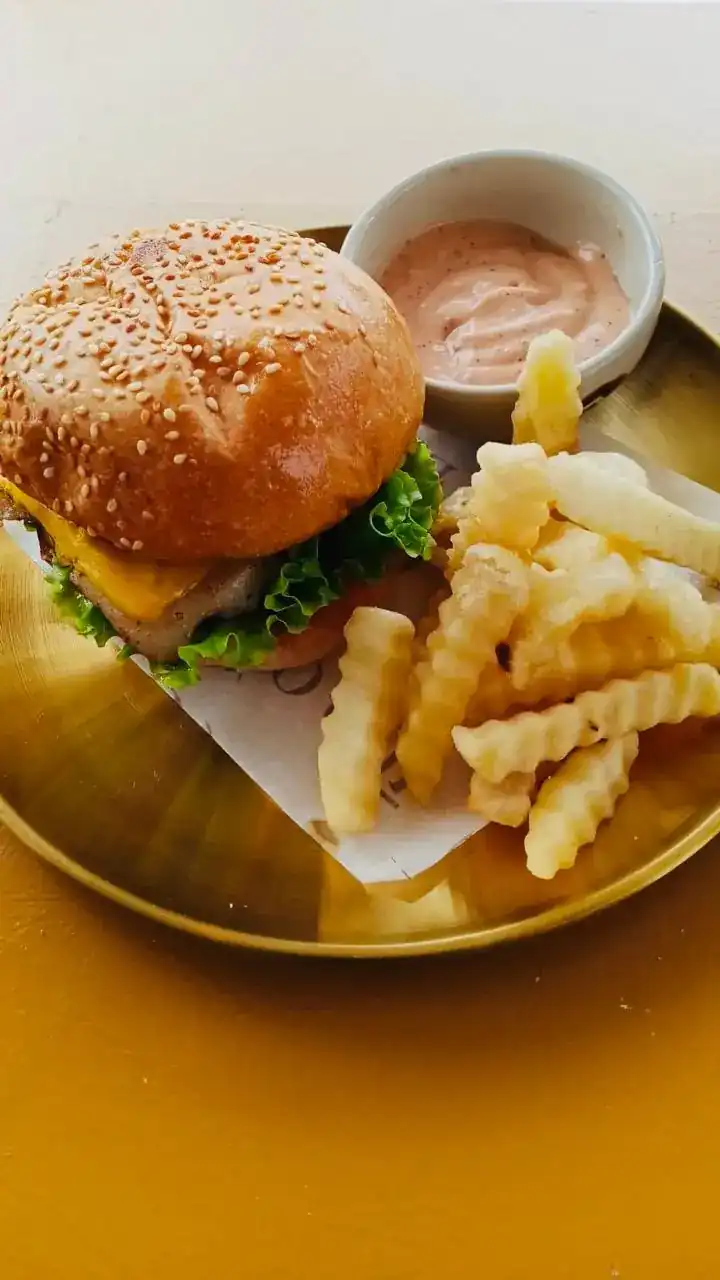 A sesame burger with cheese and lettuce next to crinkle-cut fries and a pink sauce on a gold tray
