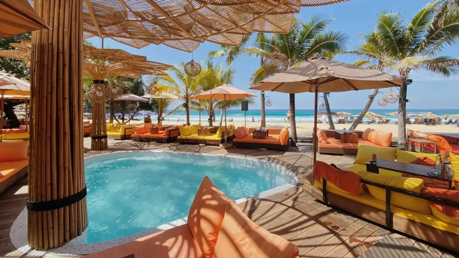Pool with orange and yellow daybeds under bamboo parasols, Karon Beach behind