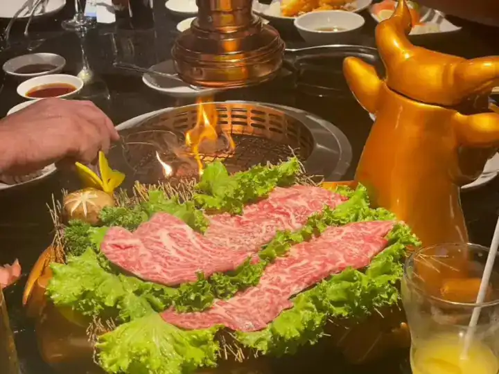 Wagyu on lettuce beside a flaming table grill, a golden bull figure on the table