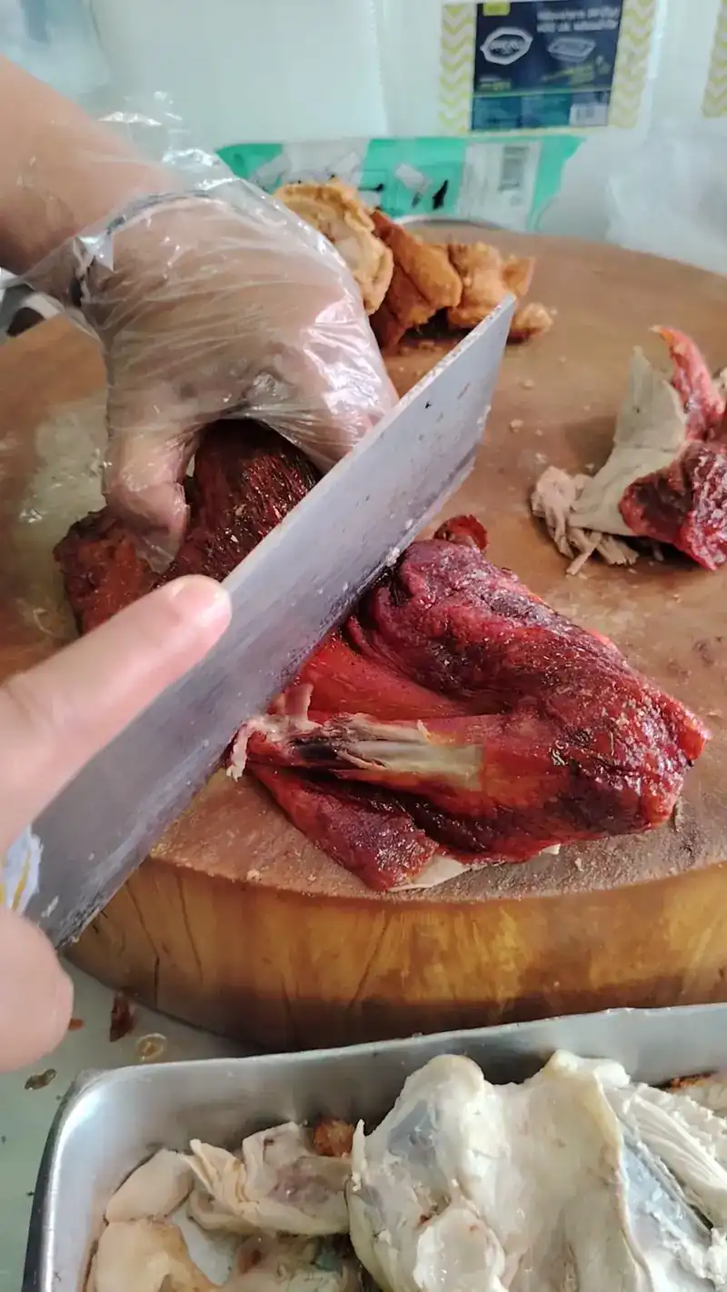 A gloved hand chopping red pork with a cleaver on a round wooden block