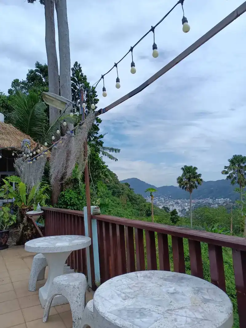 Stone tables at the wooden terrace rail, with palms and the hills and town in the valley beyond