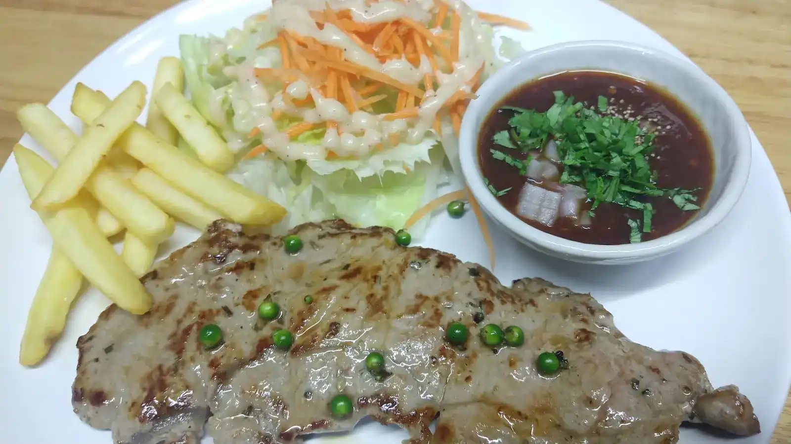 Grilled steak with green peppercorns, fries, salad and a dipping sauce