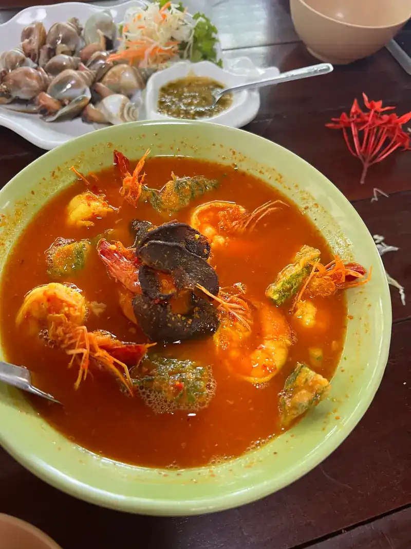 Orange sour curry with prawns, shellfish and a dipping sauce behind