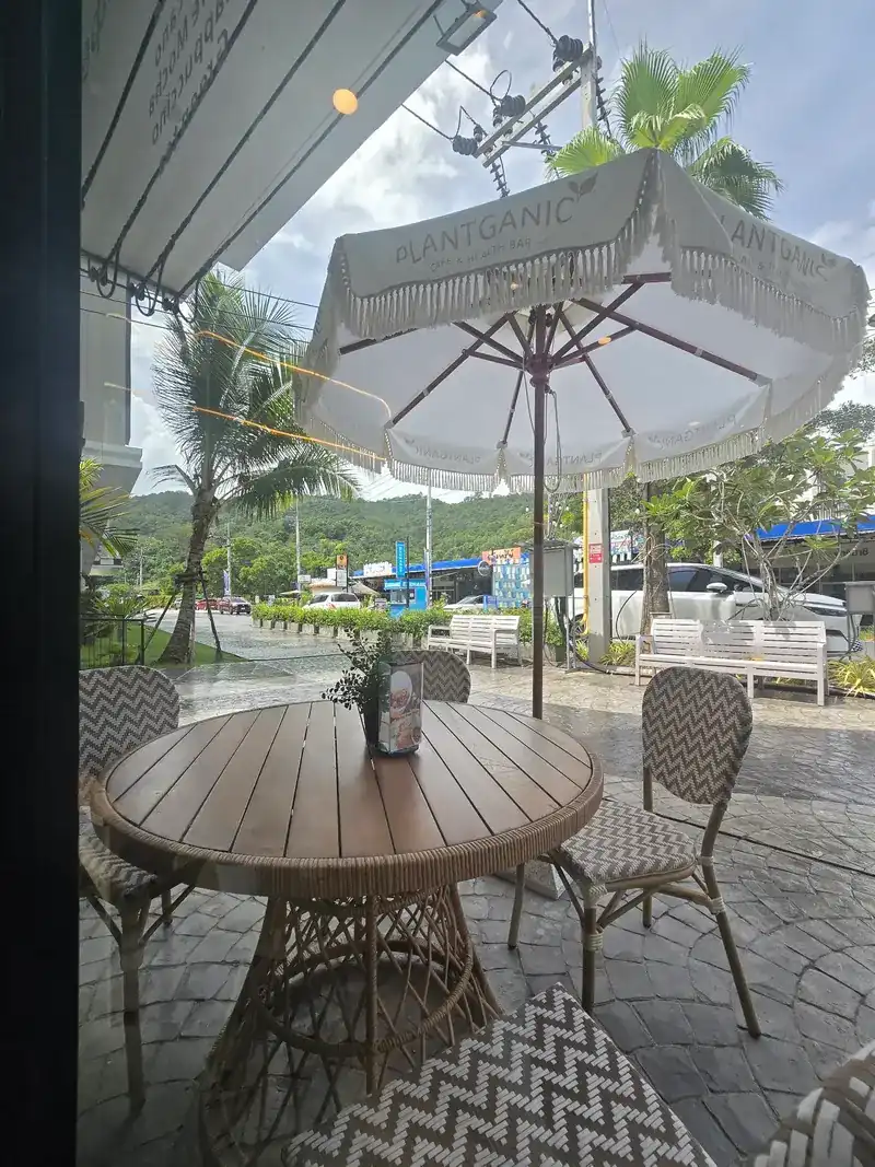 Terrace table under a white fringed umbrella, palms and the road beyond