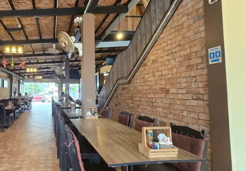 The dining room: long wooden tables beside a brick wall, fans under a woven ceiling, the street at the far end