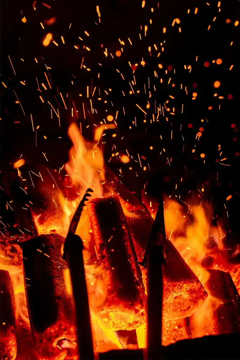 Pressed charcoal burning with sparks rising in the dark