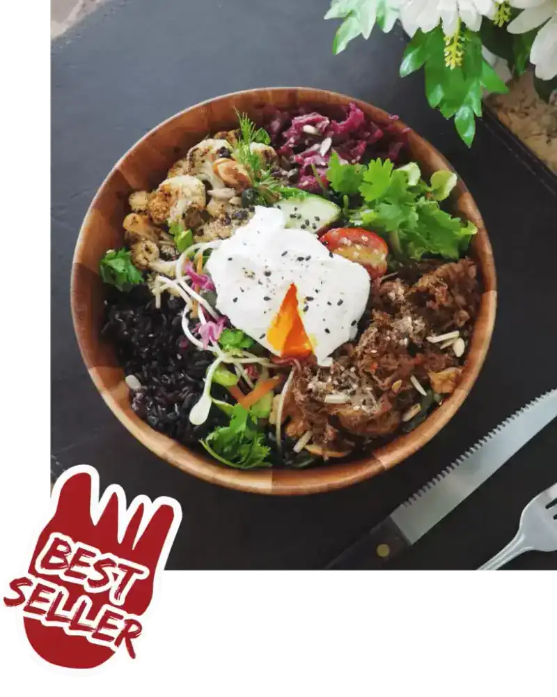 A wooden bowl with a poached egg, black rice, pulled meat, cauliflower and greens