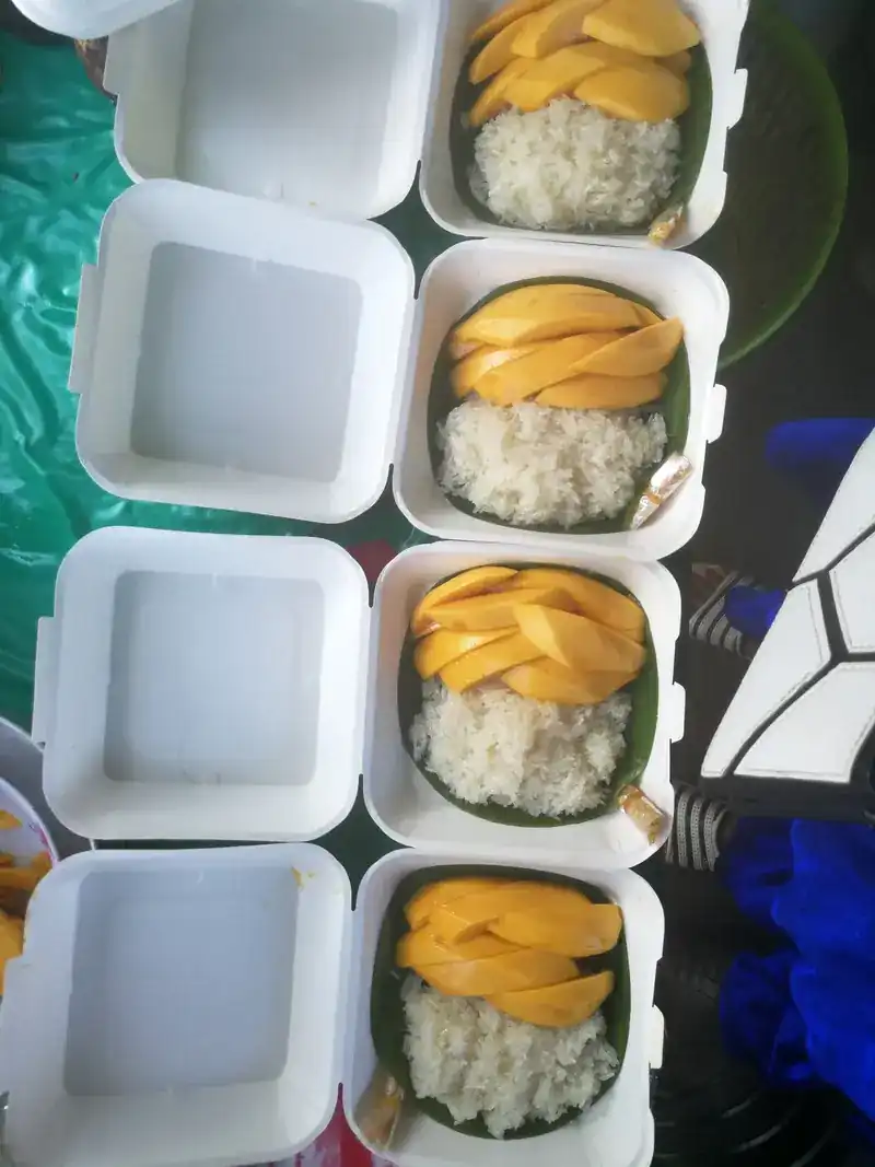White boxes open in a row, each with sliced mango and sticky rice on banana leaf