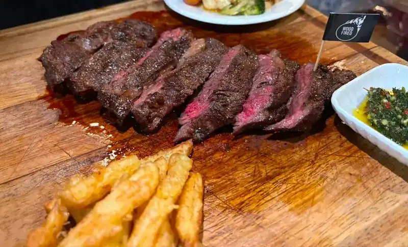 Steak sliced on a wooden board with fries and a green herb sauce