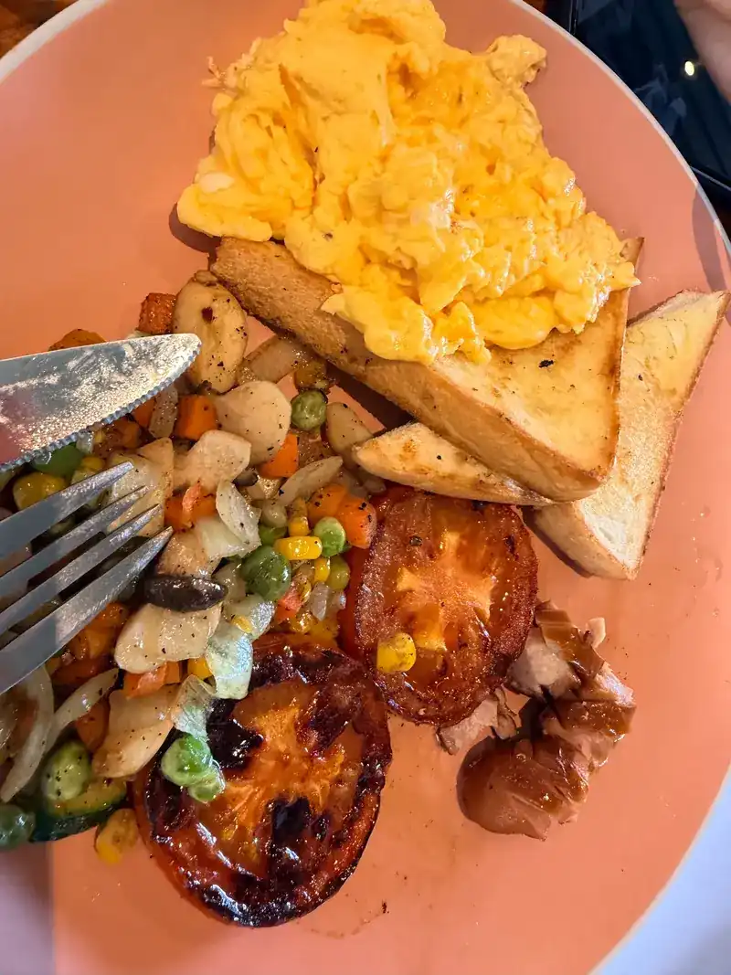 A breakfast plate with scrambled eggs, toast, grilled tomato and mixed vegetables