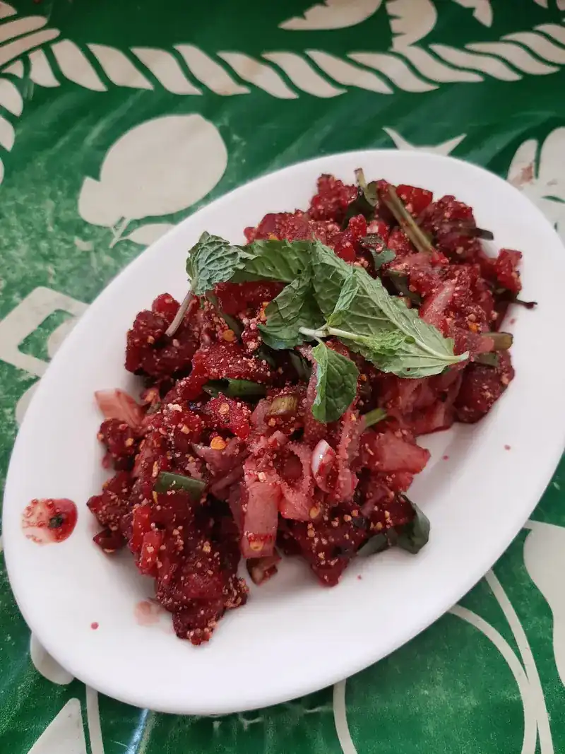A deep-red salad of chopped, spiced meat topped with mint on a white plate