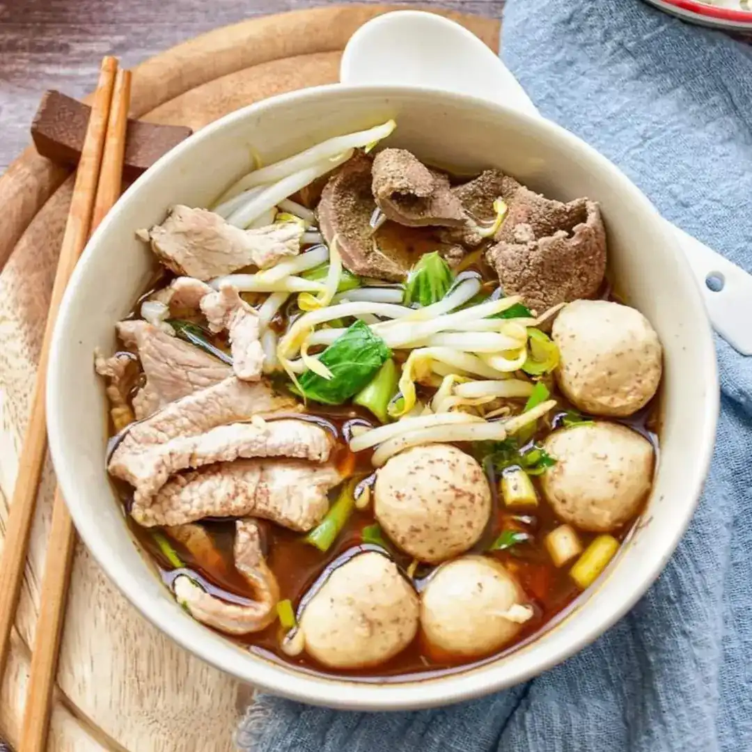 Boat noodles with meatballs, bean sprouts and greens in a dark broth