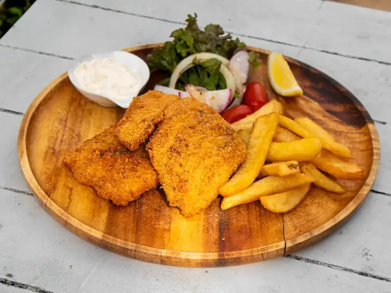 Fish and chips with salad and a creamy dip on a wooden plate