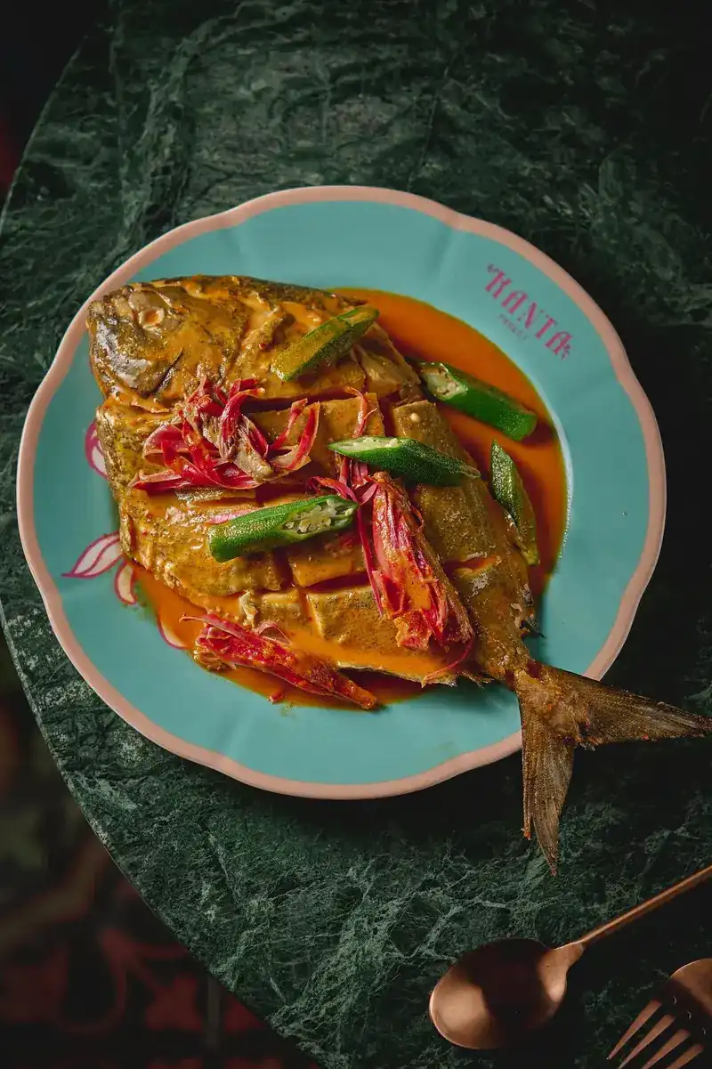 A whole fish in a rich orange sauce with okra, served on a turquoise Kanta plate