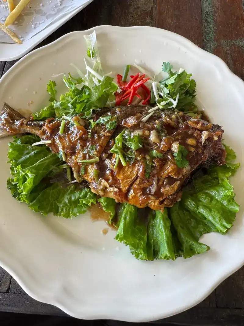 A fried fish in sauce, topped with herbs and red chilli