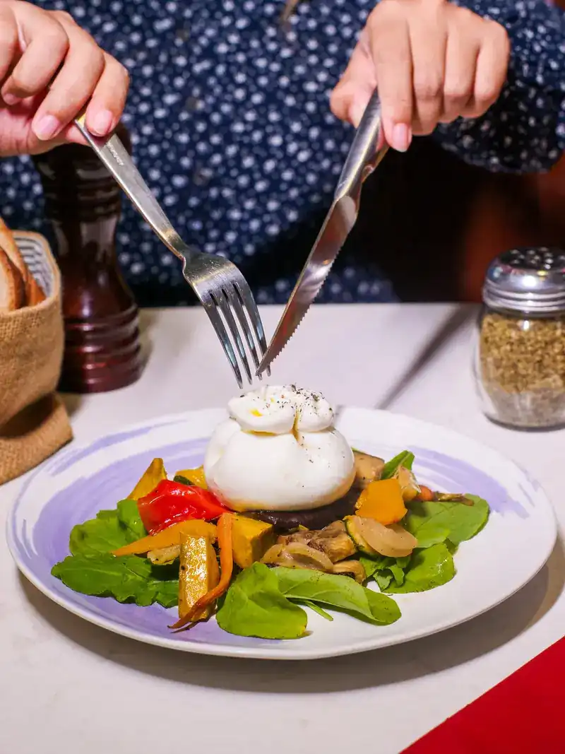 A knife and fork about to cut a ball of fresh cheese on grilled vegetables