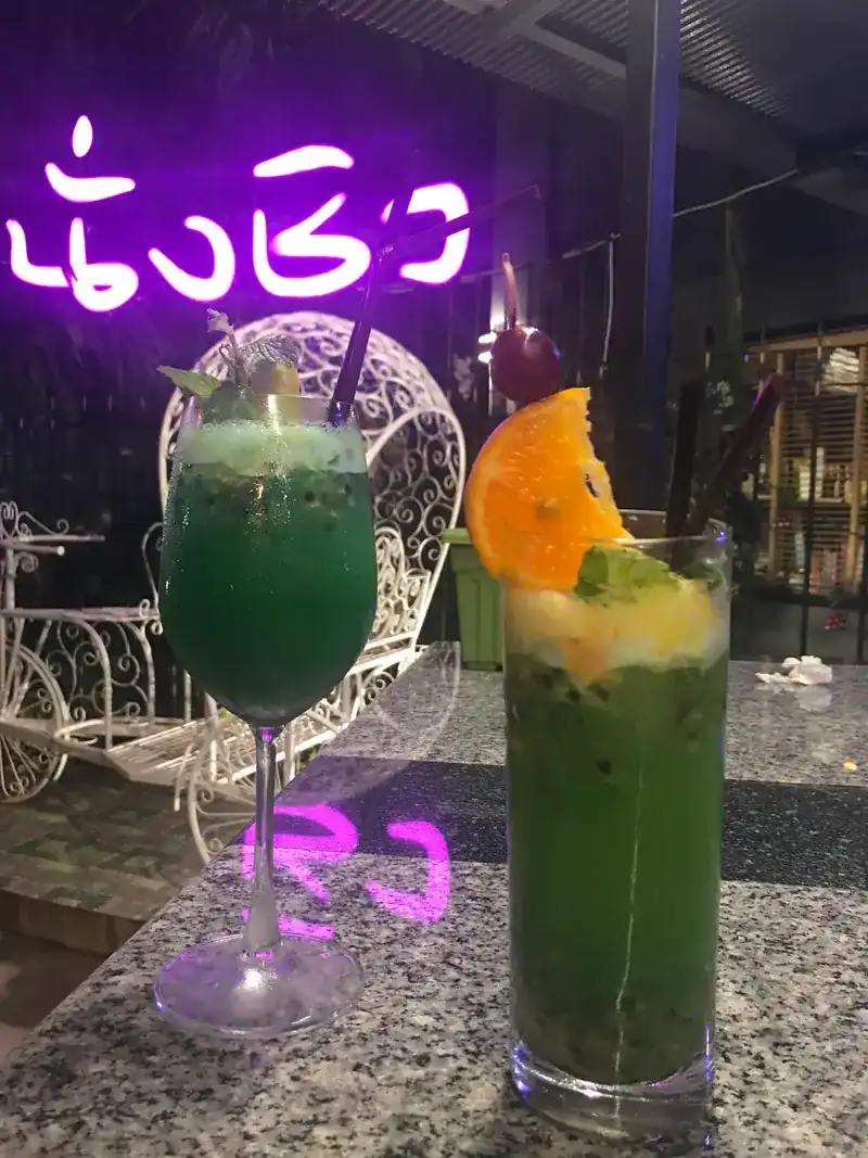Two green drinks on the granite counter under the pink neon sign