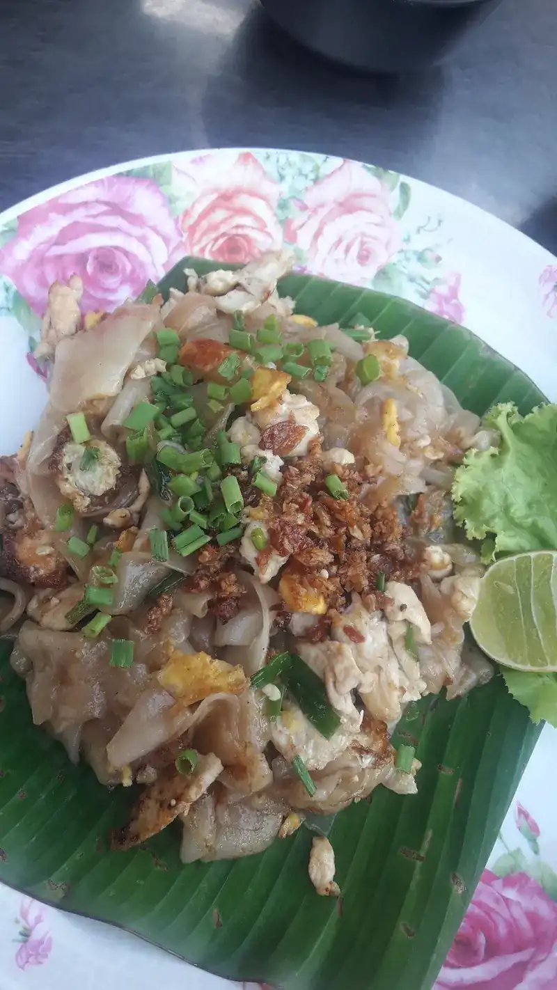 Stir-fried wide rice noodles with egg on a banana leaf, with lettuce and lime