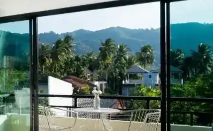 Palm trees and green hills seen from a balcony with a small table and chairs